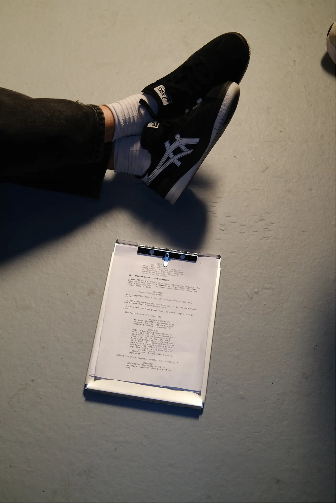 Script on a clipboard beside crossed sneakers